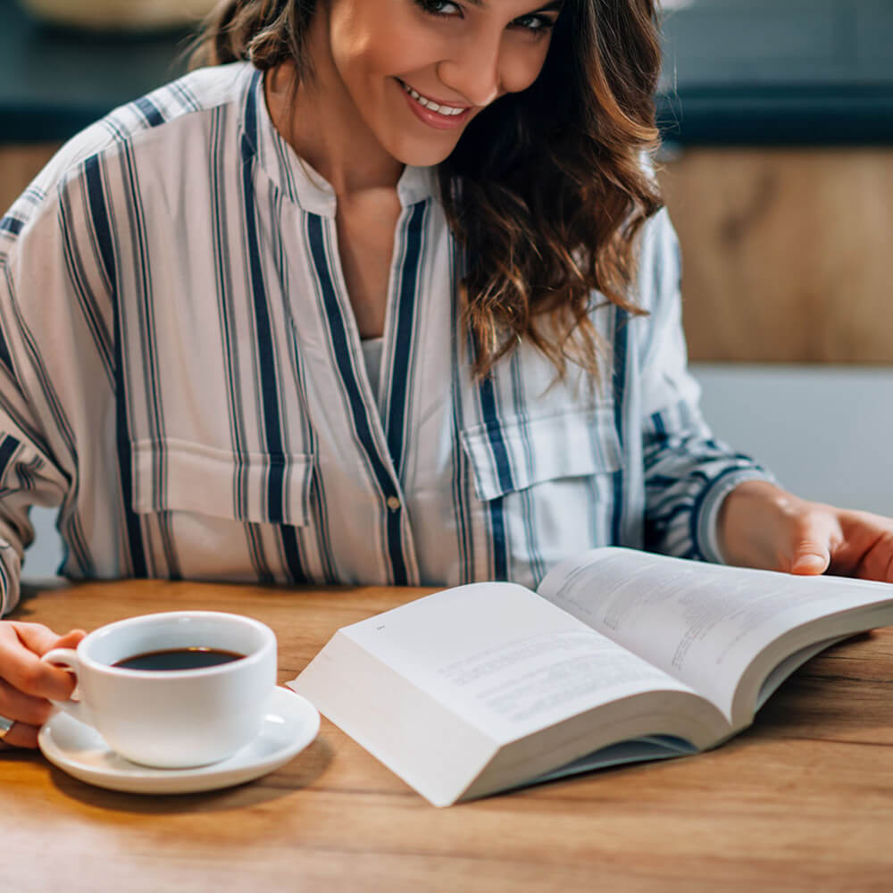 A woman smiling and drinking tea with book in her hand - Inner Oak Therapy Psychotherapy